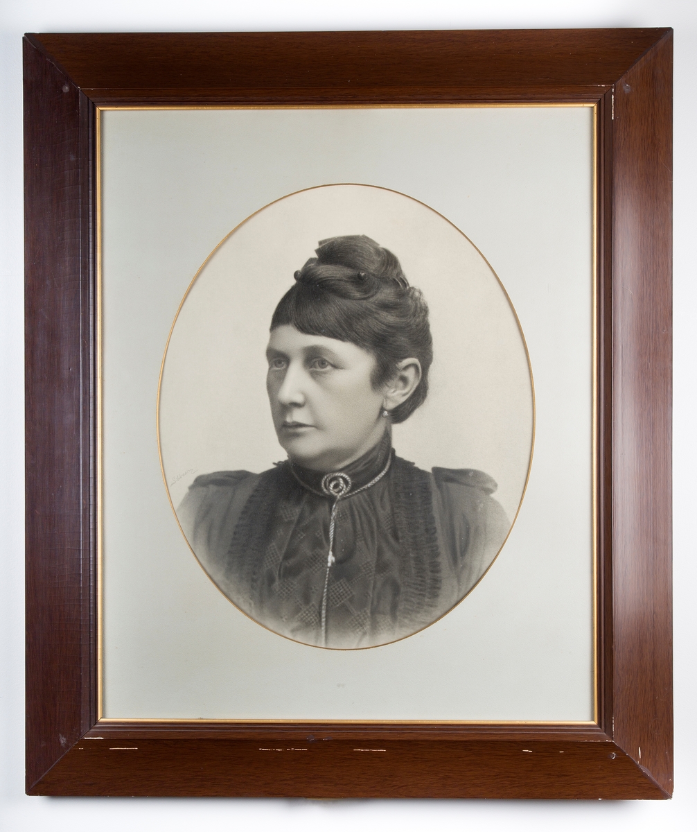 Fotografi i glass og brun ramme, rektangulær. Foto ovalt. Viser Roald Amundsens mor.