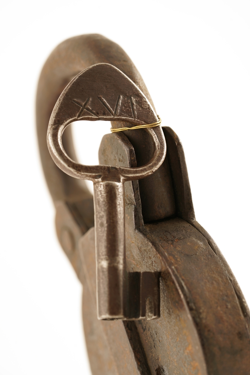 Hengelås av jern med svingbart lokk over nøkkelhull. Ova eller rund.
Nøkkel av jern. Gjennombrudt, hul, med forhøyning i nøkkelens overkant.