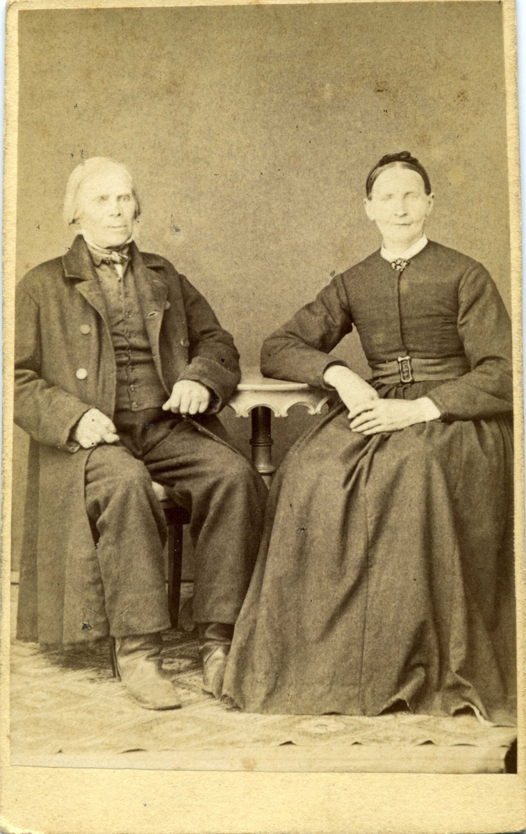 Kabinettsfotografi: ett okänt äldre par, man och kvinna, sittande vid ett bord.