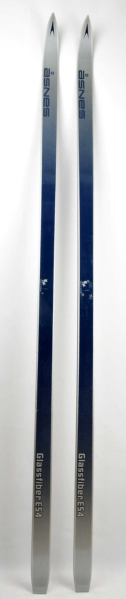 Langrennski laga av glasfiber, med såle av plast. Blå overside med striper og dekor i sølv. Det er bora hol til binding i den eine skia.   