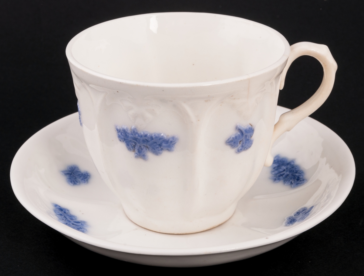 Kaffekopp med fat. 6 st. Vitt flintgodsporslin med blå druvklasar pålagda i relief.