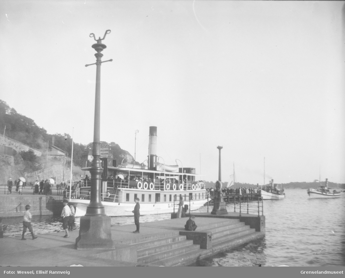 Passasjerbåten D/S Louise ligger ved kai ve Akershus festning, ca 1900. Mennesker på brygga og flere båter på vei inn.