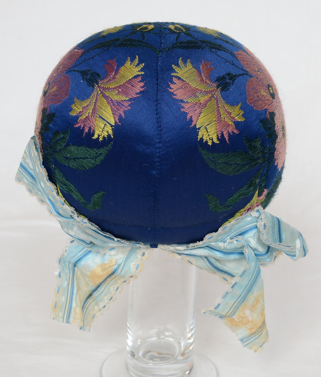 Huvudbonad för kvinna, bindmössa, blå med invävda blom- och blad- mönster i gult och rött.
