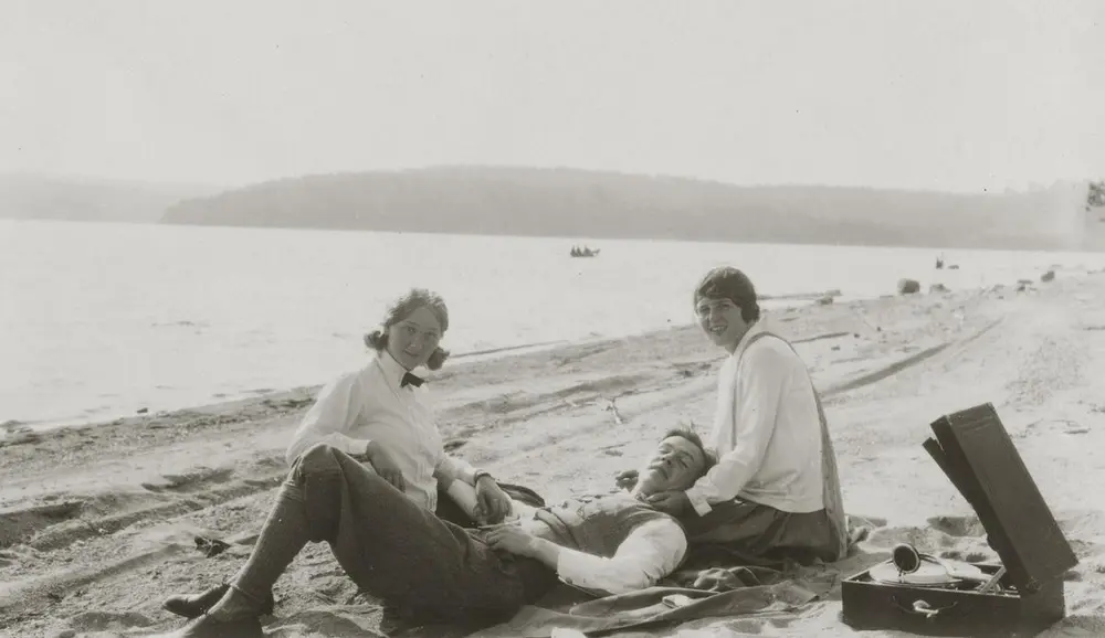 To kvinner og en mann hører på musikk fra en platespiller på stranden. Foto: MiA.