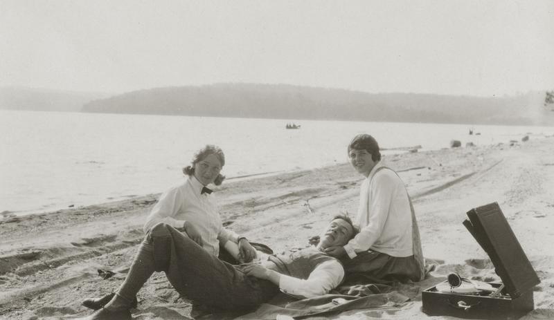 To kvinner og en mann hører på musikk fra en platespiller på stranden. Foto: MiA.
