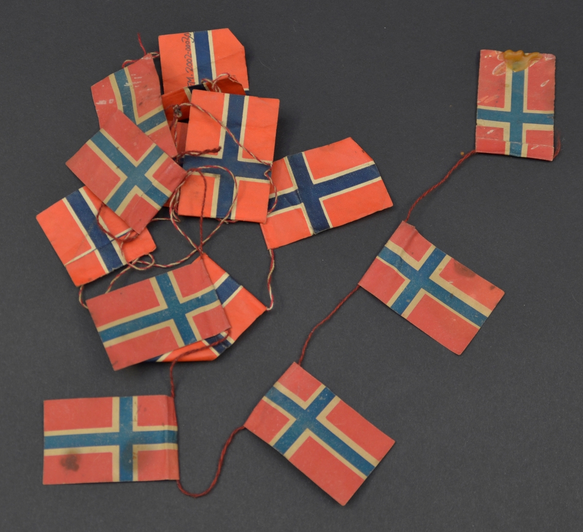 Lekkje med norske flagg, sett saman av to ulike typar. Den eine typen har klårare fargar enn den andre og snor som er tvunne av raud og kvit tråd. På den andre typen er snora tvunne av to raude trådar.
