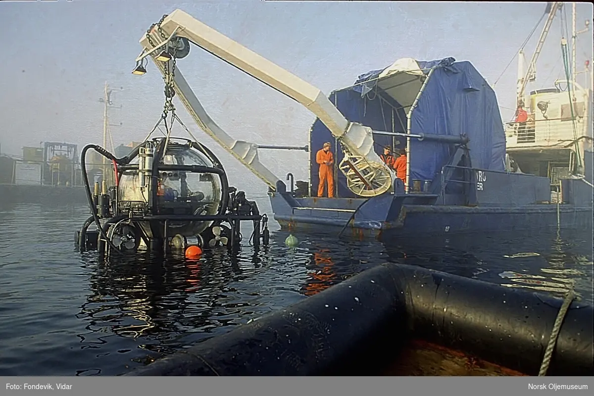 Miniubåten Check Mate fra "NUTEC" med to personer i er heises opp eller ned av vannet. Den henger i kranbommen på dykkerbåten "Strilborg", senere omdøpt til "Deepsea Inspector".