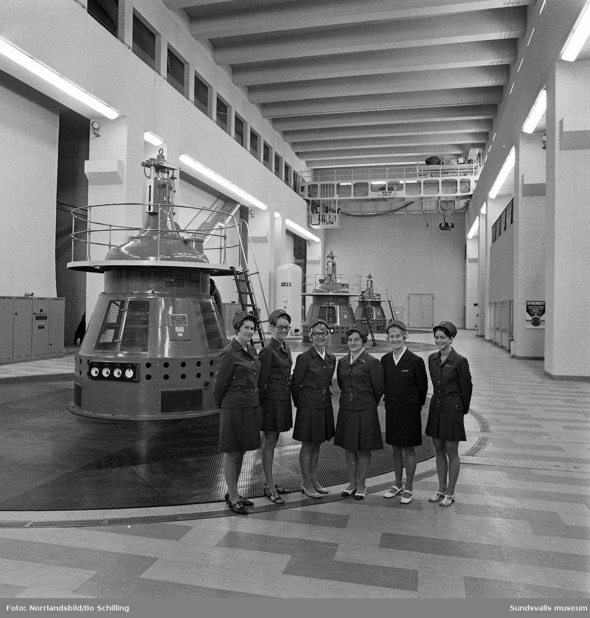 Sex kvinnor i uniform samt en man vid en manöverpanel på Bergeforsens kraftverk. Fotograferat för en affisch.