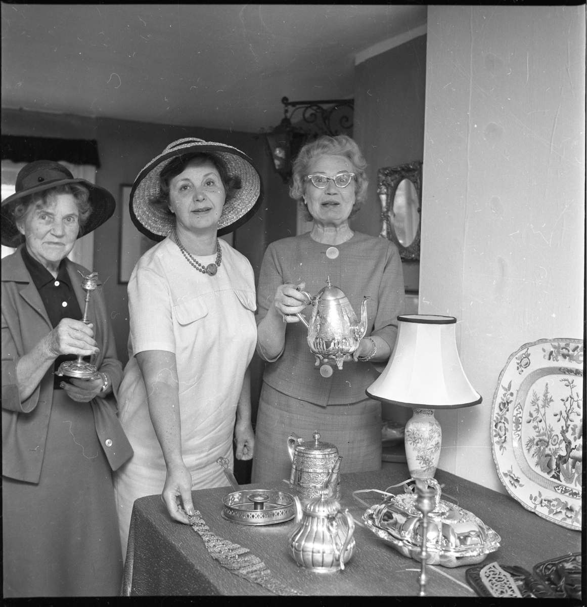 Ella Rudman och två oidentiferade kvinnor med hatt vid bord med äldre silverföremål.