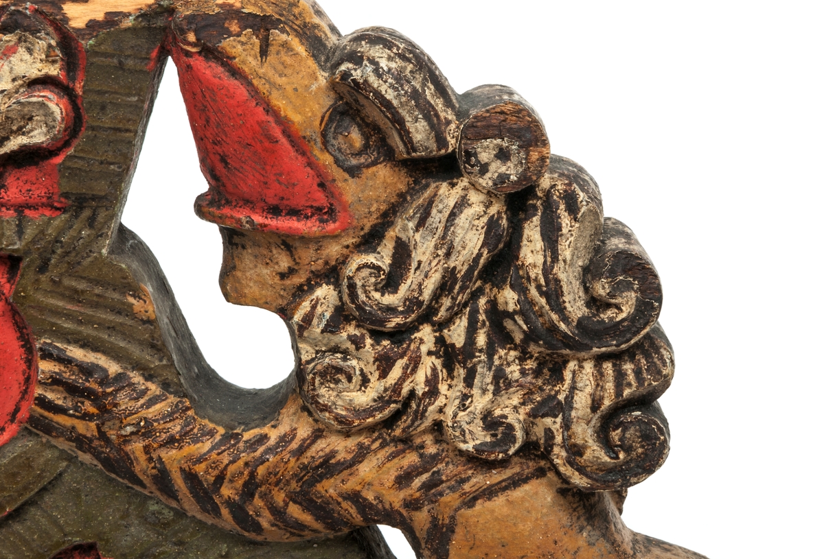 Selkrok av trä, skulpterad och målad i rött, grönt och brunt. Skulpteringen föreställer två lejon hållande ett kronliknande ornament.