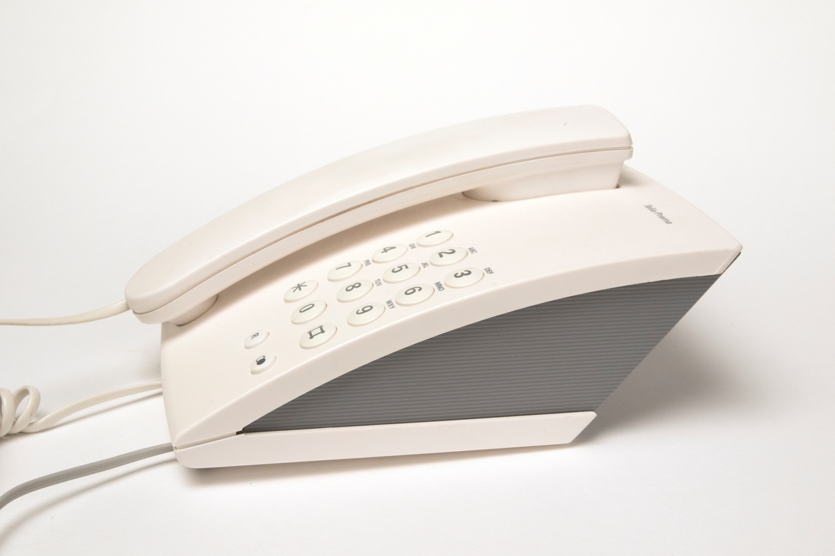 Telefon, tonvalstelefon för bords- eller väggplacering av vit och grå plast. Telefonen är trådbunden och försedd med plastsladd.