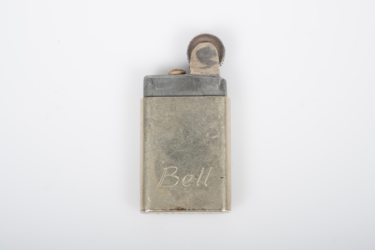 Fyrtøy i lysgul metall med inngravert navn "Bell" på nederdelen.