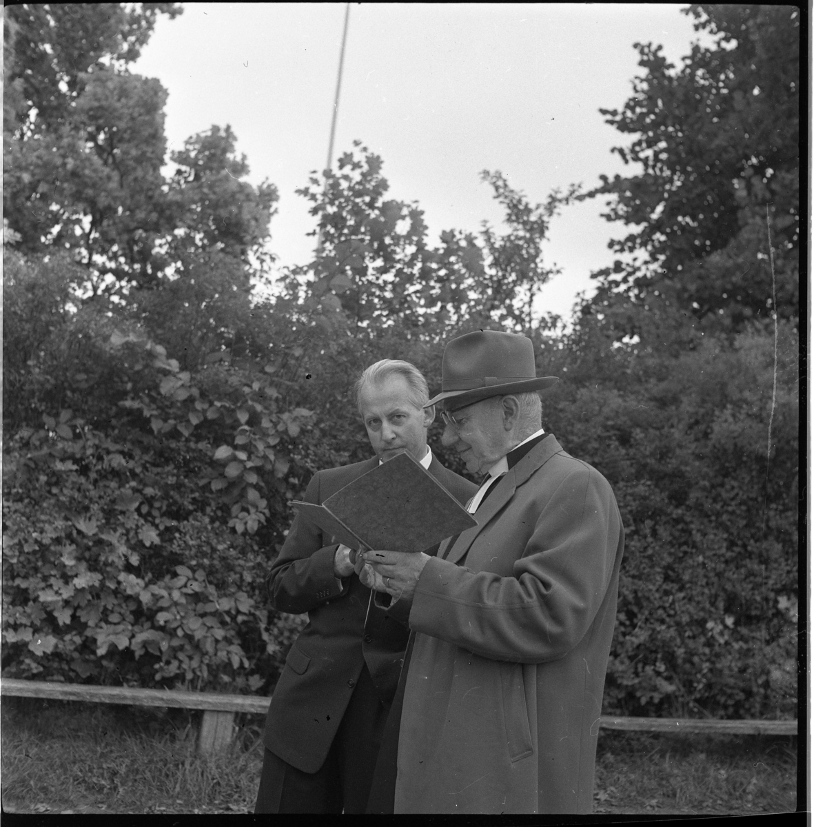 Kyrkoherde Ernst Sandgren till höger i samtal med okänd man utanför Ölmstad prästgård i samband med konfirmationsträff i Ölmstad (1932 års konfirmander), de tittar i en bok.