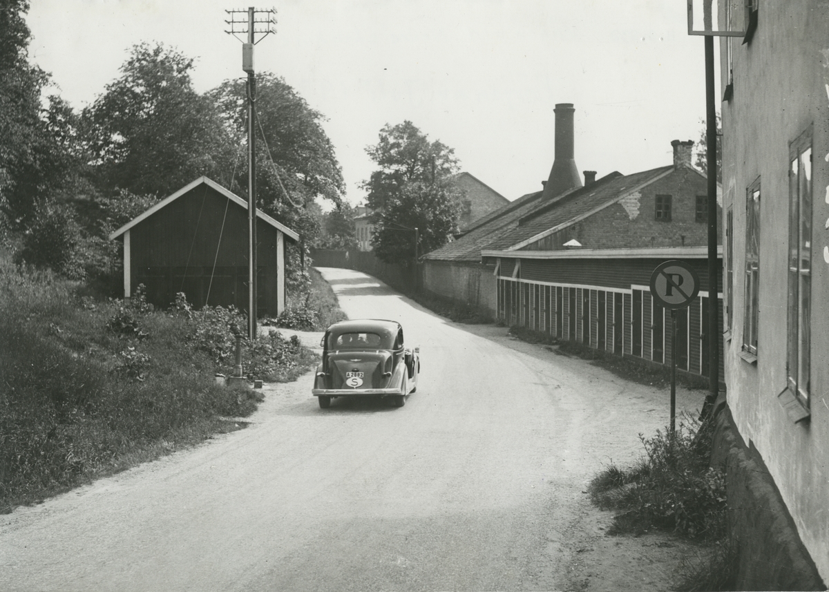 Exteriörbild. Bil vid Algatan, nuvarande Gustavsbergsvägen/Gustavsbergs Allé. Nedre Stenhuset till höger. Längs Algatan avträden och äldre fabriksbyggnader. Bild fotad före 1945. Byggnaderna bortöver är bl a huset för tegelslagning och Formgjuteriet.