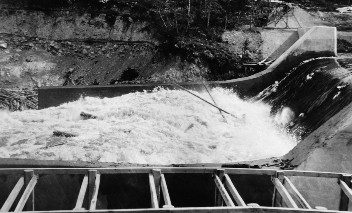 Den såkalte «Nydammen» i elva Søndre Osa i Åmot i Hedmark.  Her ble det i perioden 1912-1914 bygd et for sin tid stort kraftverk som skulle utnytte energien i Osfallet. Dammen som magasinerte vann til dette kraftverket brast under en plutselig vårflom i 1916, som forårsaket betydelige skader.  Den opprinnelige dammen lot seg ikke gjenoppbygge. I stedet ble det oppsatt en ny dam i det nye løpet som vannmassene fra dambruddet hadde skapt. Denne dammen var en betongkonstruksjon.  På dette fotografiet ser vi hvordan vannet, etter å ha passert damkrona, dannet en kvitskummende masse over ei «golving» nedenfor fallet. I disse kvitskummende vannmassene skimter vi en del fløtingstømmer. I forgrunnen skimtes en del trekonstruksjoner i noe som later til å ha vært en kanal ved siden av tømmerløpet. Dette kan ha vært ei fisketrapp.