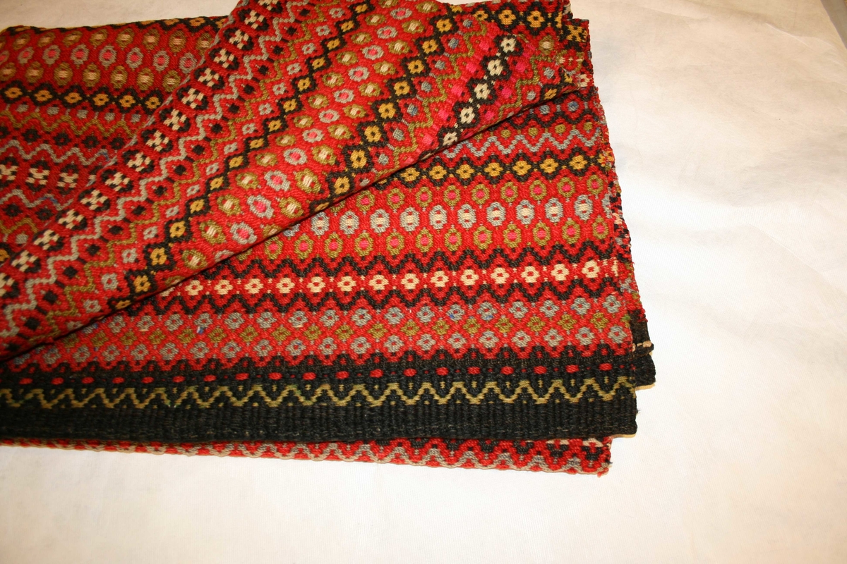 Rektangulært ullteppe med mønster, sydd saman av 2 breidder, falda  i båe endar.