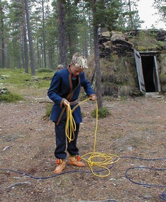 Samisk gutt i tradisjonelle samiske klær som surrer sammen en gul lasso.