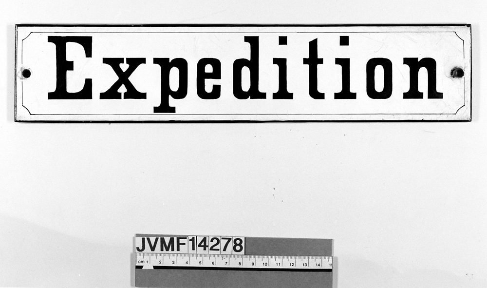 Långsmal skylt av plåt med svart text på vit botten:
"Expedition".