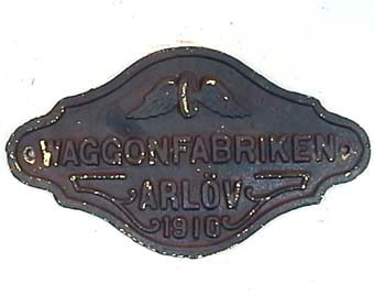 Svart skylt med gul text, nu mestadels bortnött. Text: "Waggonfabriken Arlöv 1910".