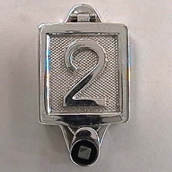 Fyrkantig vändbar skylt som kan låsas med fyrkantnyckel.
Skylten är av förnicklad, silverfärgad mässing med siffror i relief mot räfflad botten.
På ena sidan står det:
"1".

På andra sidan står det:
"2".