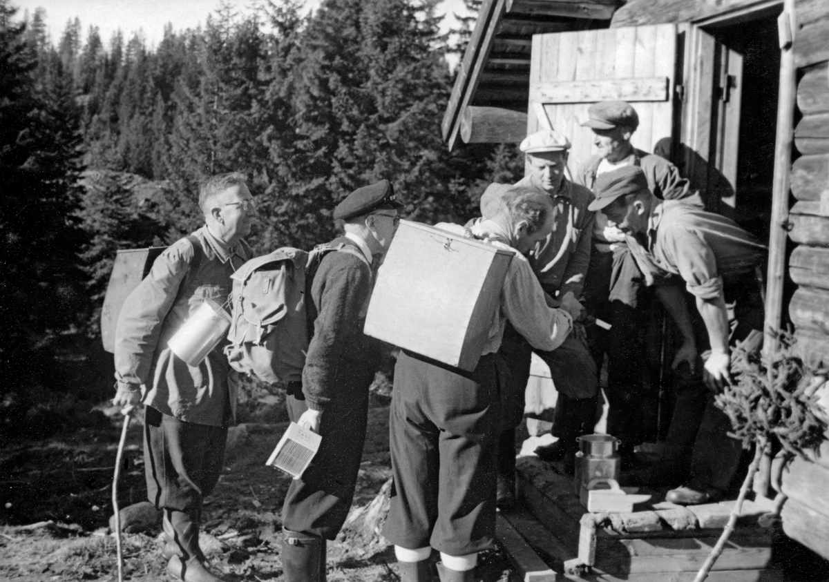 Bærtur i området ved Gullverket i Eidsvoll en høst i perioden 1950-52.  Bildet viser seks menn, kledd og utstyrt for plukking av skogsbær, framfor et laftehus med inngangsdør på gavlveggen, muligens ei koie.  Et par av karene bar spesiallagde bærkasser av tre på ryggen, andre hadde ryggsekker og blikkspann til å samle bæra i.  En av karene holdt en bærsanker i hånda.

Mannen lengst til venstre på bildet er Knut Øsmundset (1891-1977), som har lagd ei bærkasse som er overlatt til Norsk Skogmuseum (SJF.13704). Da dette fotografiet ble tatt hadde han det nevnte bæreredskapet på ryggen.
