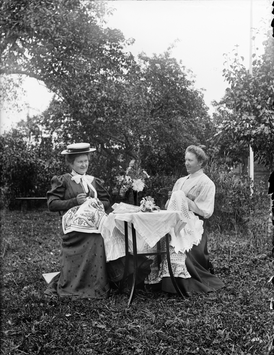 Karin Arnell och Anna Alinder sitter i trädgården och handarbetar, Uppland i början av 1900-talet