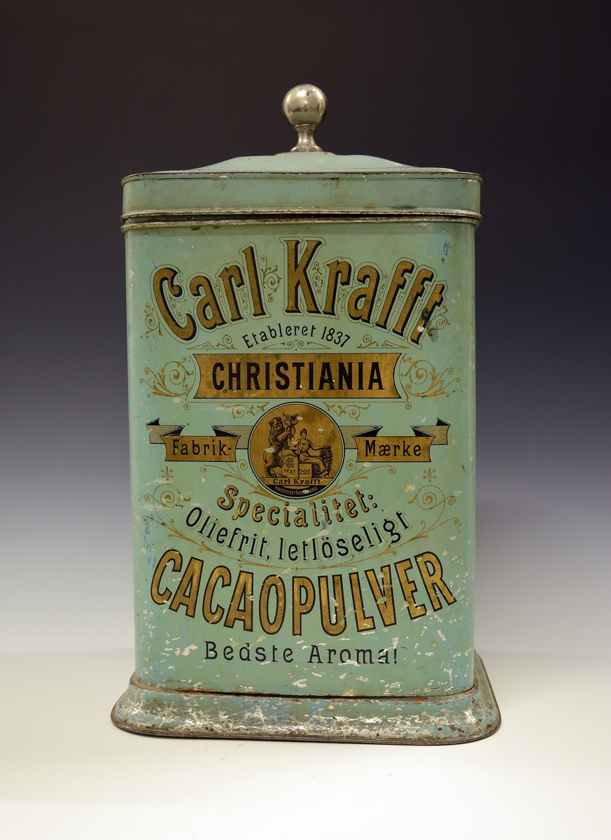 Kakaoboks i blikk, rektangulær med avrundede hjørner og lokk med blank knott. Fra Carl Krafft, Christiania.