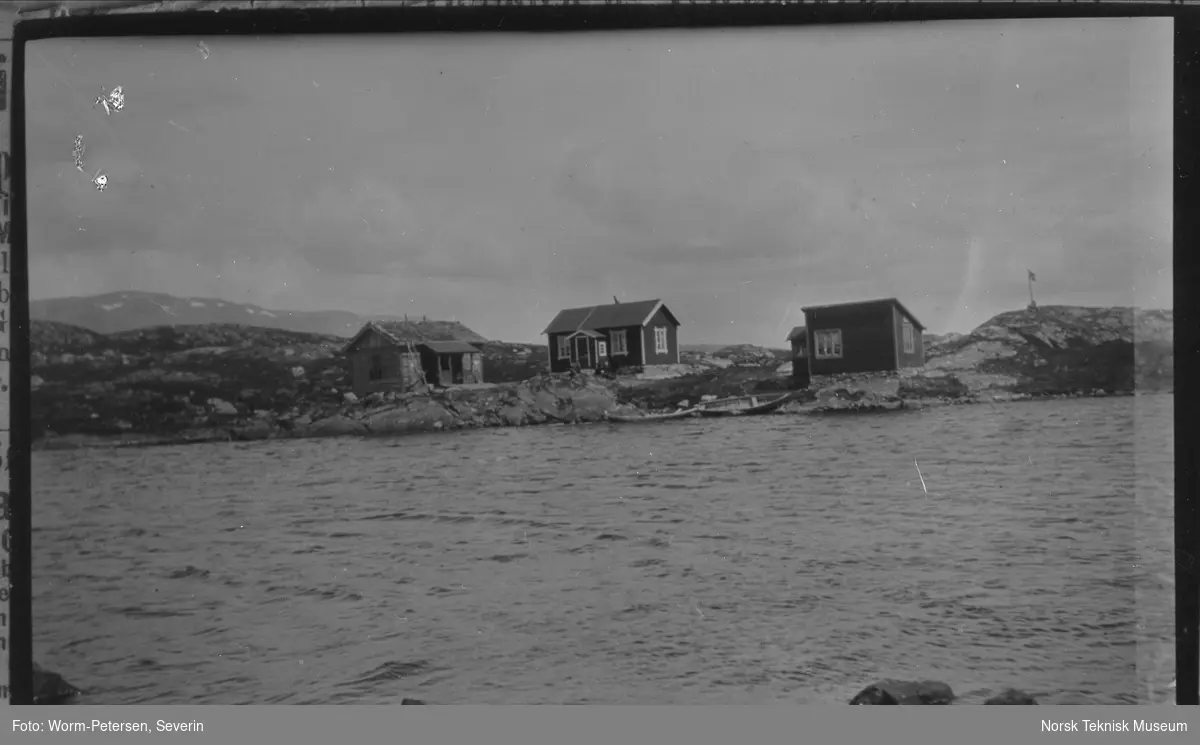 Avstandsbilde av tre små hus ved sjøen