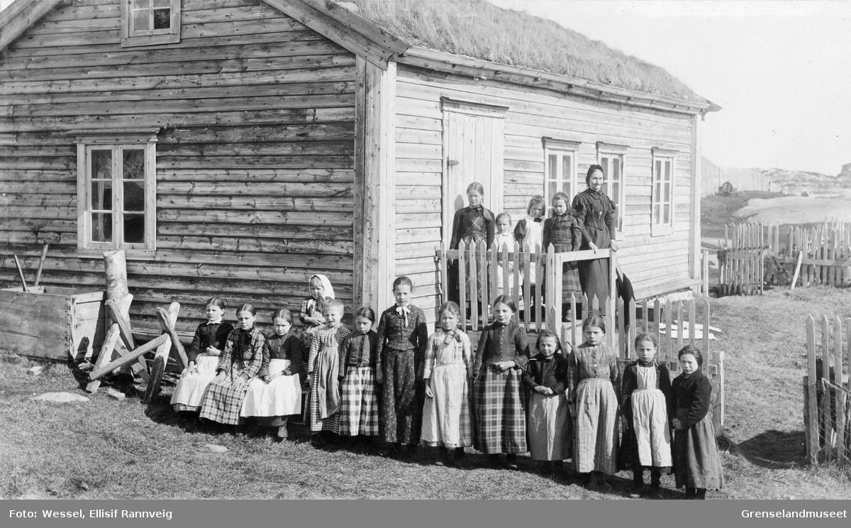 Handgjerningsskolen med kvenske jenter i Bugøynes, 1898. Lærerinne fru Pernille Hee står på trappen. Huset ble solgt til Aage Pleym og ombygget. 