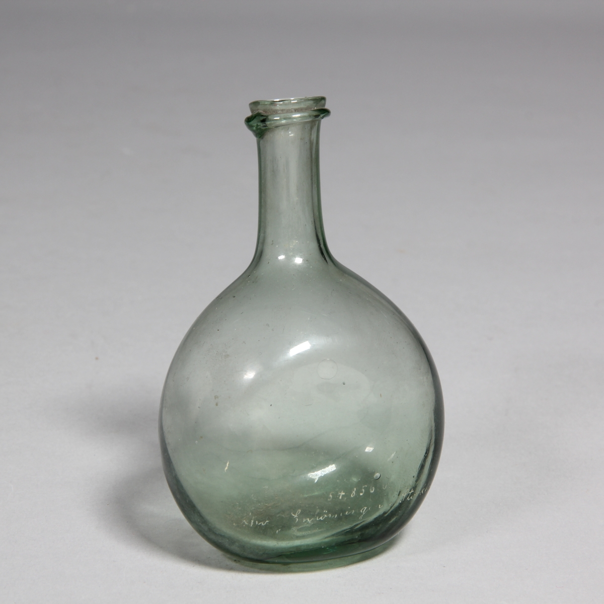 Flaska av grönt glas, rund med tillplattade sidor, lång hals.