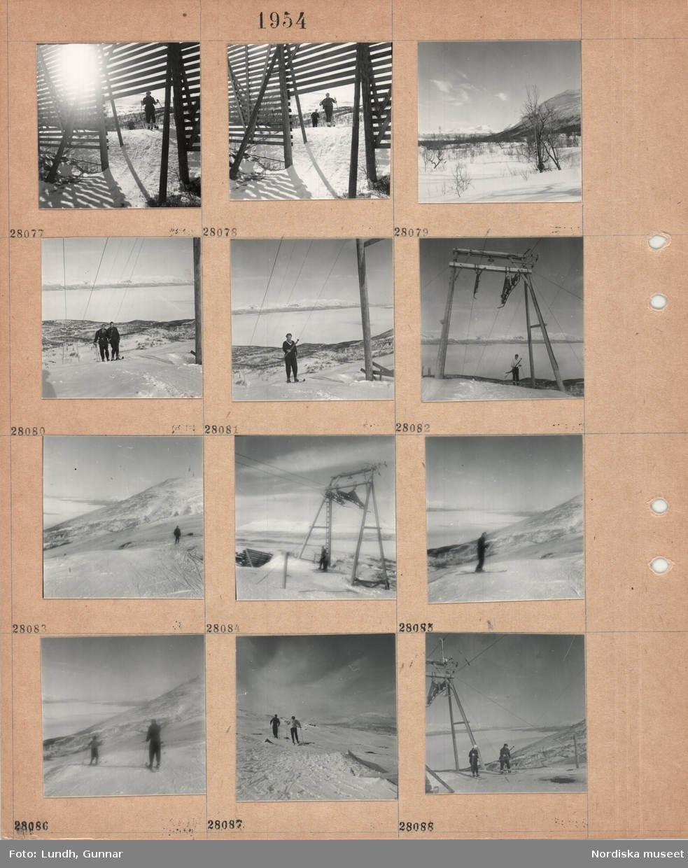 Motiv: (ingen anteckning) (Abisko) ;
Ett snöstaket med skidåkare i bakgrunden, en snötäckt landskapsvy med skog och fjäll, två personer åker i en lift - en släplift, två personer åker skidor på ett fjäll.