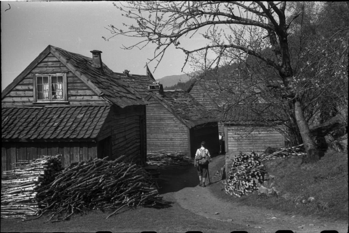 Bilder av en gård og en mann som går inn på gårdsplassen med tursekk og turstav.