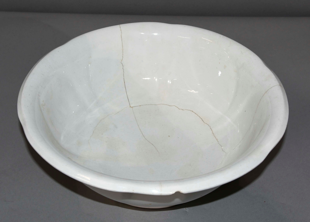 Vaskevannsfat av hvit keramikk. Rund form med helletut. Keramikken har sprekker.
