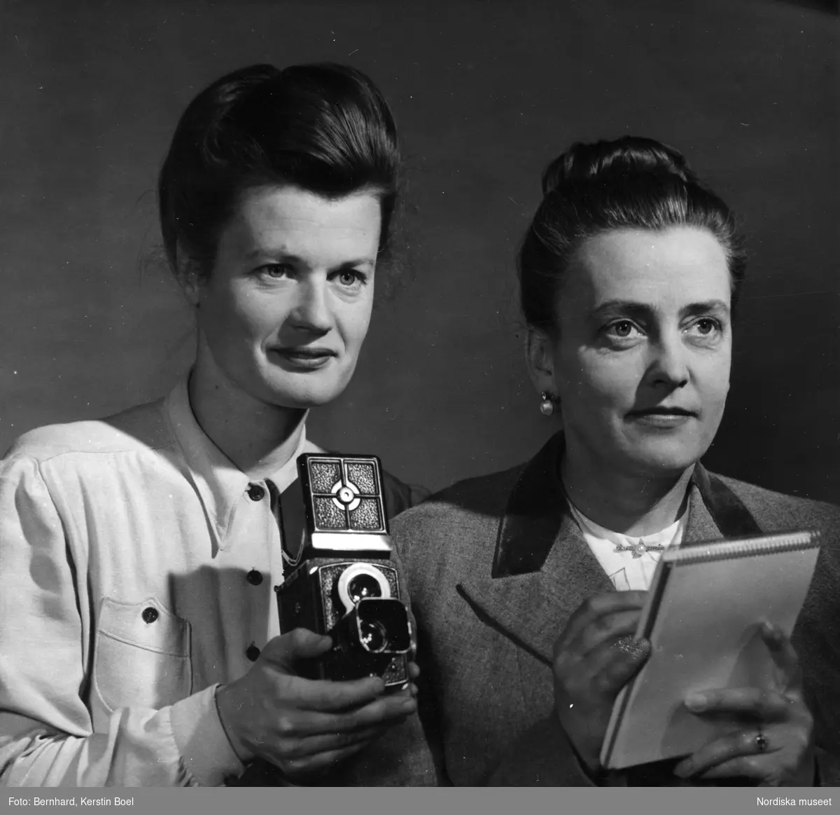 Fotografen Kerstin Bernhard hållandes en Rolleiflex-kamera och journalisten Ingrid af Ström hållandes ett notisblock