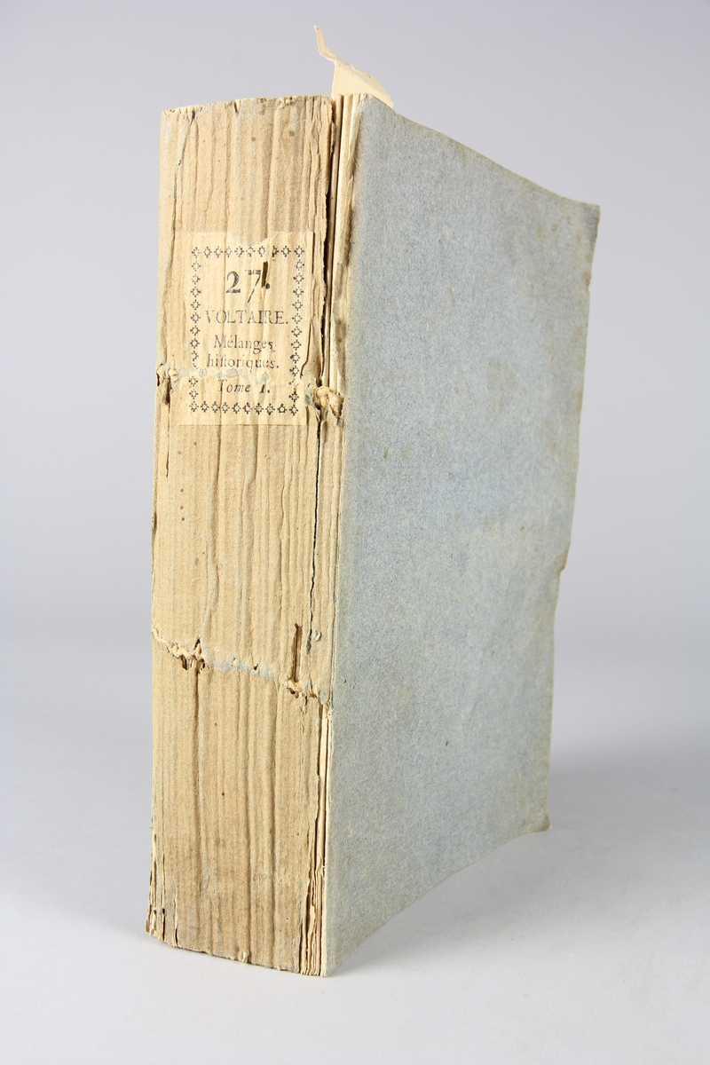 Bok, pappband,"Oeuvres completes de Voltaire", del 27,  "Melanges historiques", del 1.
Pärmen klädd med gråblått papper, skurna snitt. På ryggen klistrad pappersetikett med tryckt text samt volymens nummer. Ryggen blekt.