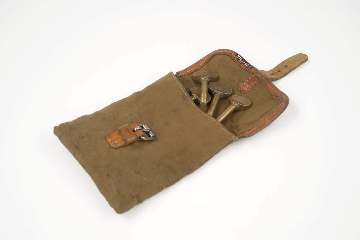 10 messingskruer pakket i en lerretspose som lukkes med en nedbrettsflik og låses med rem og spenne