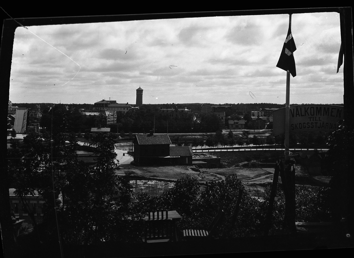 Utsikt från ett fönster ut över Trollhättan med bland annat stadens vattentorn i bakgrunden. I fotografens egna anteckningar står det: "Resa Trollhättan - Lilla Edet."