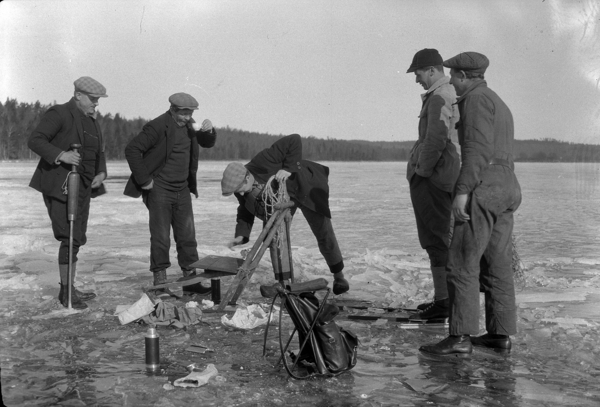 Fem män vinterfiskar och dricker kaffe. Bredvid dem på isen syns en spark, ryggsäckar och en termos. Mannen med ispiken är Olle Pettersson.