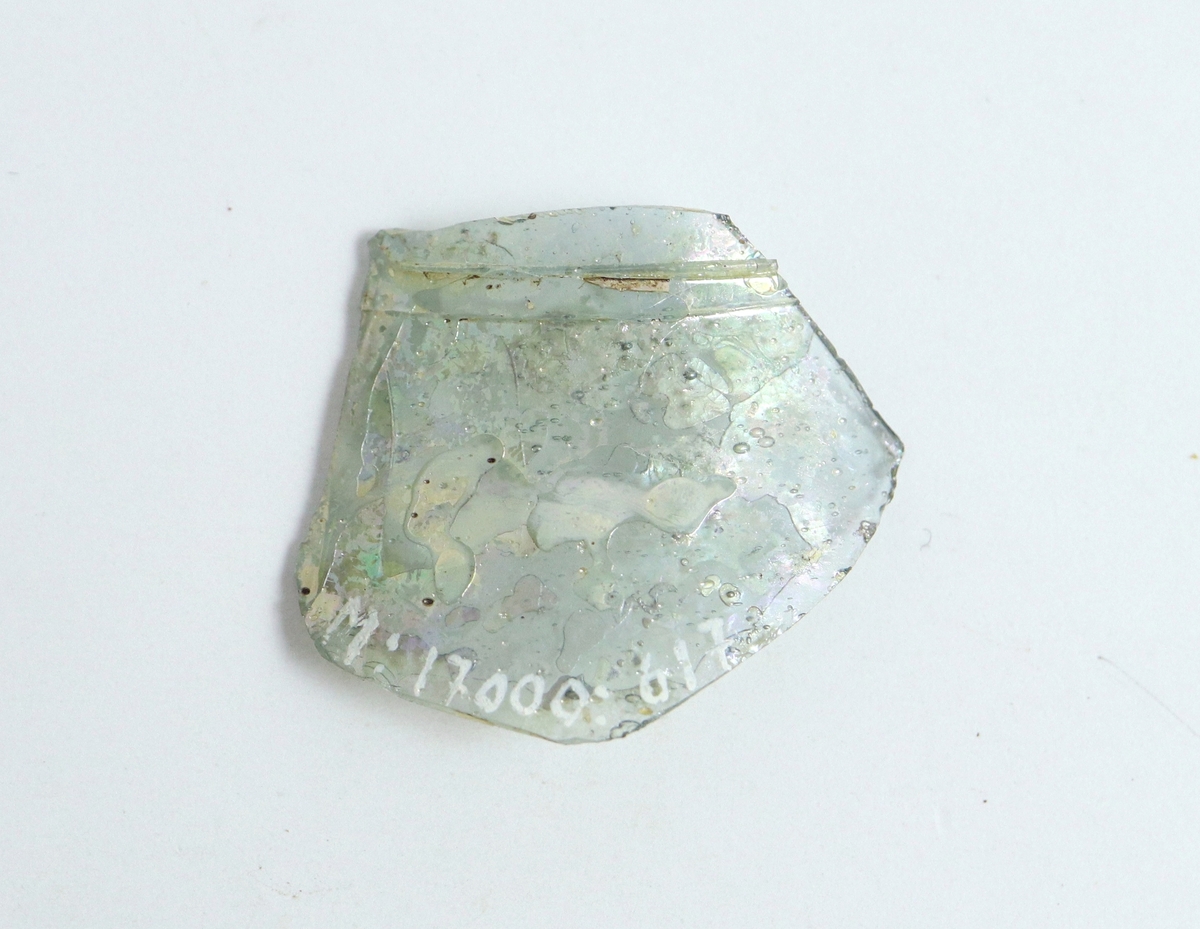 Fragment av ett cylinderformat passglas av svagt blåtonad, nu iriserande glasmassa. Cylinderformat kärl med pålagd tråd. Mycket lik M 17000-633.