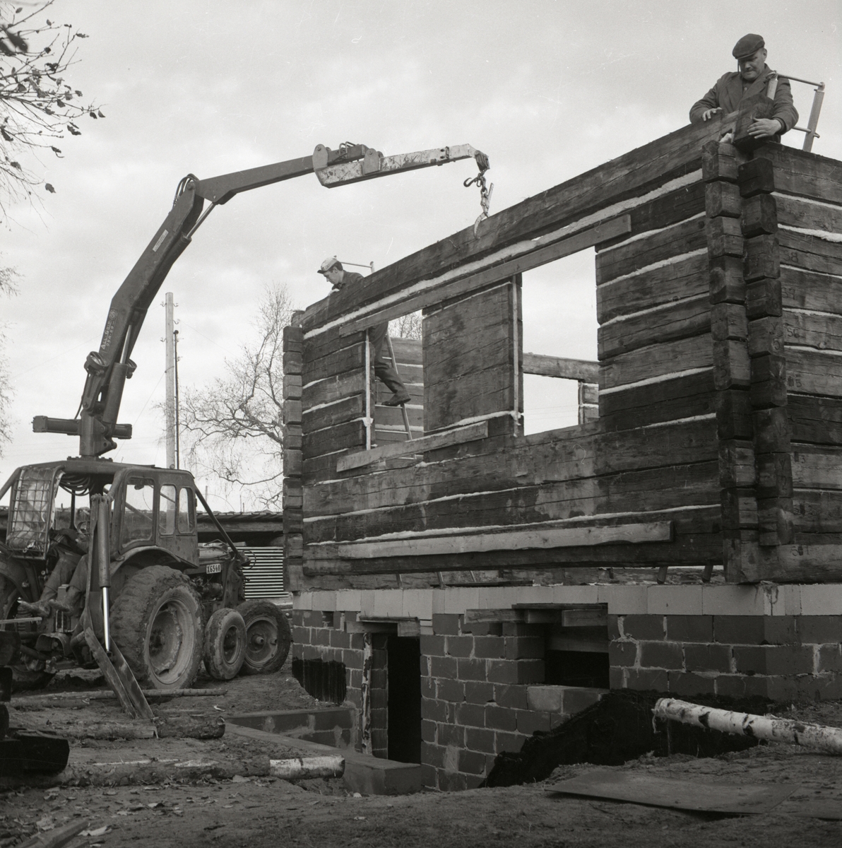 Ett nytt bostadshus av timmer monteras ihop med hjälp av en traktor vid gården Sunnanåker, 1967.