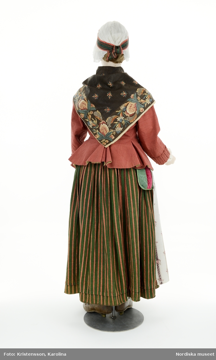 Prästfrun 1780, från utställningen Modemakt. Modellen är fotograferad för 360-visning. Information om kläderna se Relaterade objekt under Referenser. Strumpor, rosettknytning tröja och veckat stycke på mössan är rekvisita.