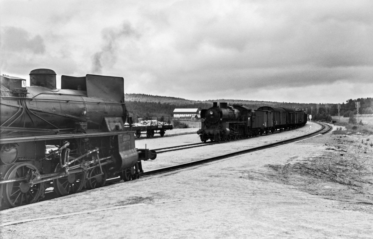 Kryssing på Os stasjon mellom godstog 5712 til Tynset og dagtoget fra Oslo Ø til Trondheim over Røros, tog 301. Godstoget trekkes av damplokomotiv type 26c nr. 399, tog 301 trekkes av type 26c nr. 413.