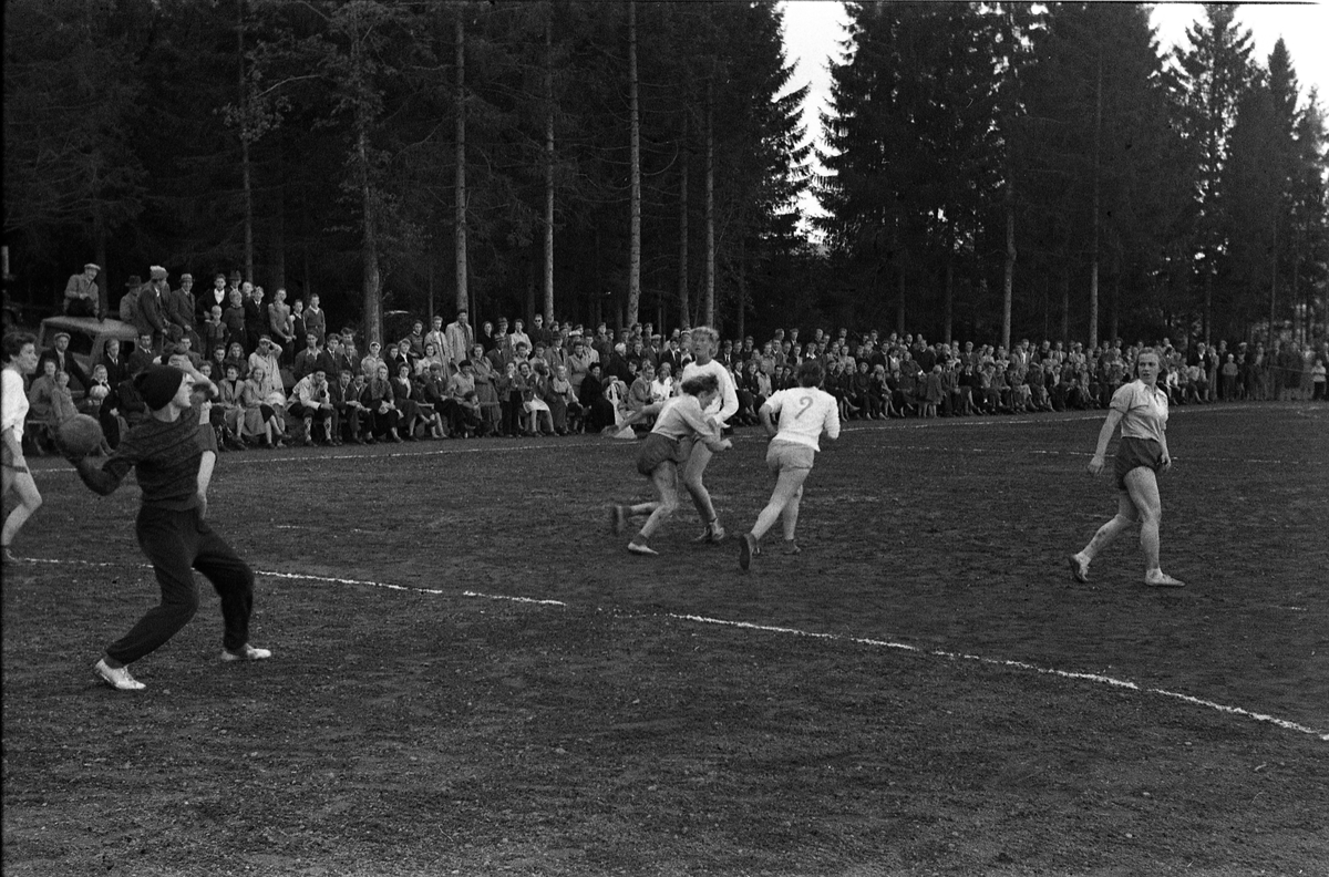 Håndballkamp på Kraby Idrettsplass september 1953. Kampen var kvartfinale i damenes Norgesmesterskap mot Nornen fra Bergen, en kamp Kraby vant og dermed kvlifiserte seg for semifinale. Krabys spillere, i de mørkeste buksene, er identifisert, men for navn henvises til lagbilde TMF-06483.
14 bilder som viser kampsituasjoner og publikum.
