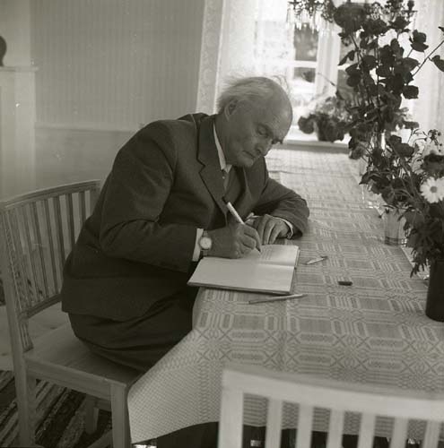 Författaren Albert Viksten sitter vid ett bord och skriver i en bok, Glössbo 1968.