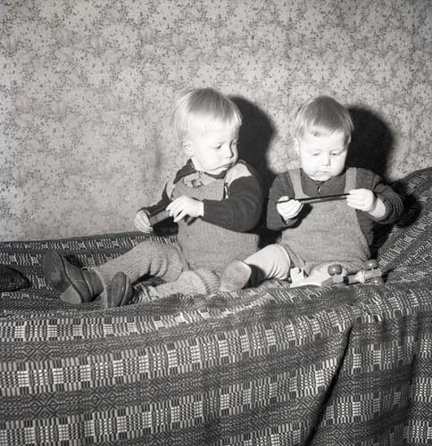 Två pojkar sitter på en säng och leker med leksaker, 1950.