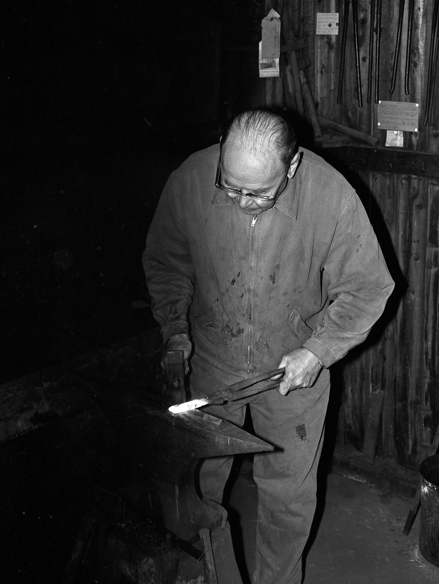 Knivmakeren Even Johannes Blindingsvolden (1908-1985) fra Ringsaker, fotografert ved ambolten i smia, der han bearbeidet glødende knivblademne med en hammer mens han holdt det med ei tang.  Den på dette tidspunktet 65 år gamle håndverkeren var kledd i dongeriklær mens han arbeidet. Blindingsvolden eide og bodde på småbruket Rudsland på Rudshøgda.  Her hadde han et et 43 kvadratmeter stort hus ved Prestvegen som inneholdt smie- og verkstedrom.

Mer informasjon om knivsmeden Even Blindingsvolden finnes under fanene «Bildehistorikk» og «Opplysninger».
