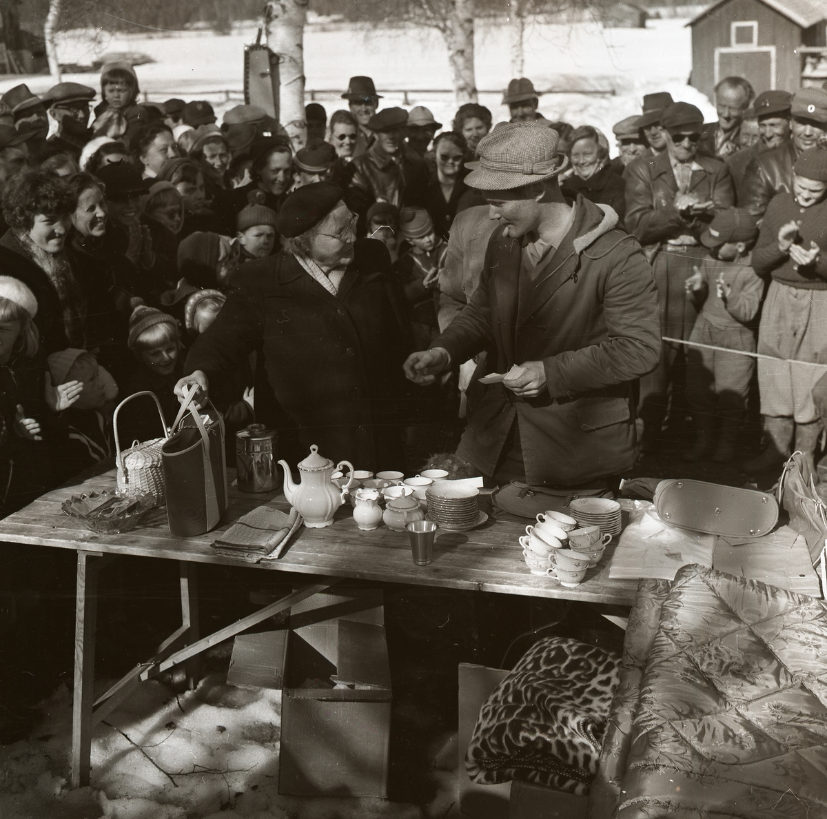 Prisutdelning vid impeltävling på Hölesjön 22 april 1956. Pristagare och publik samlas kring bordet med vinster.