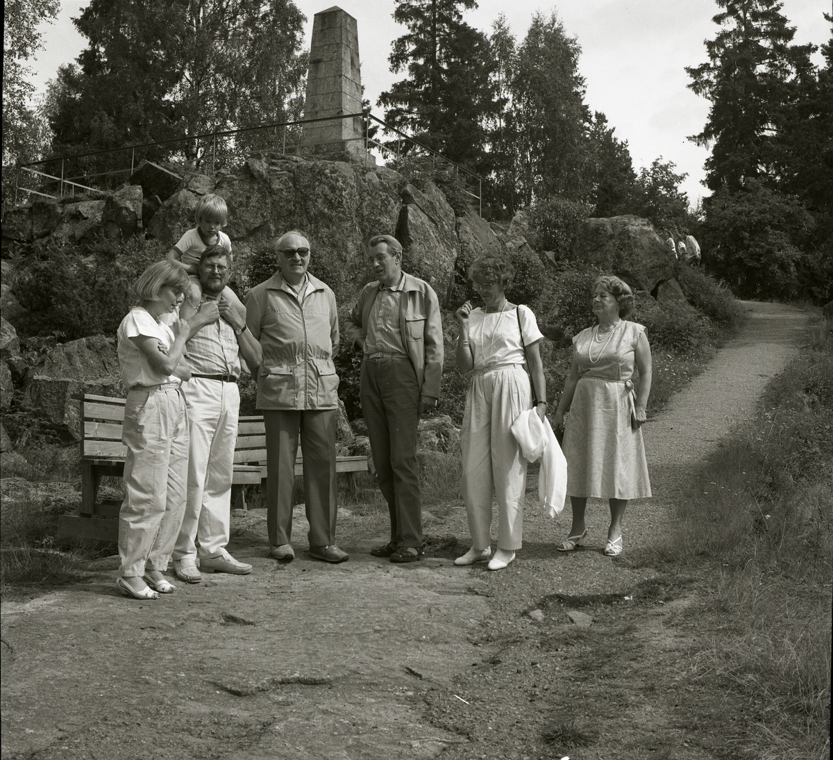Adéle, t h i bild, står med en grupp vuxna och barn på en gångväg nedanför ett slags monument, 25-29 juli 1985.