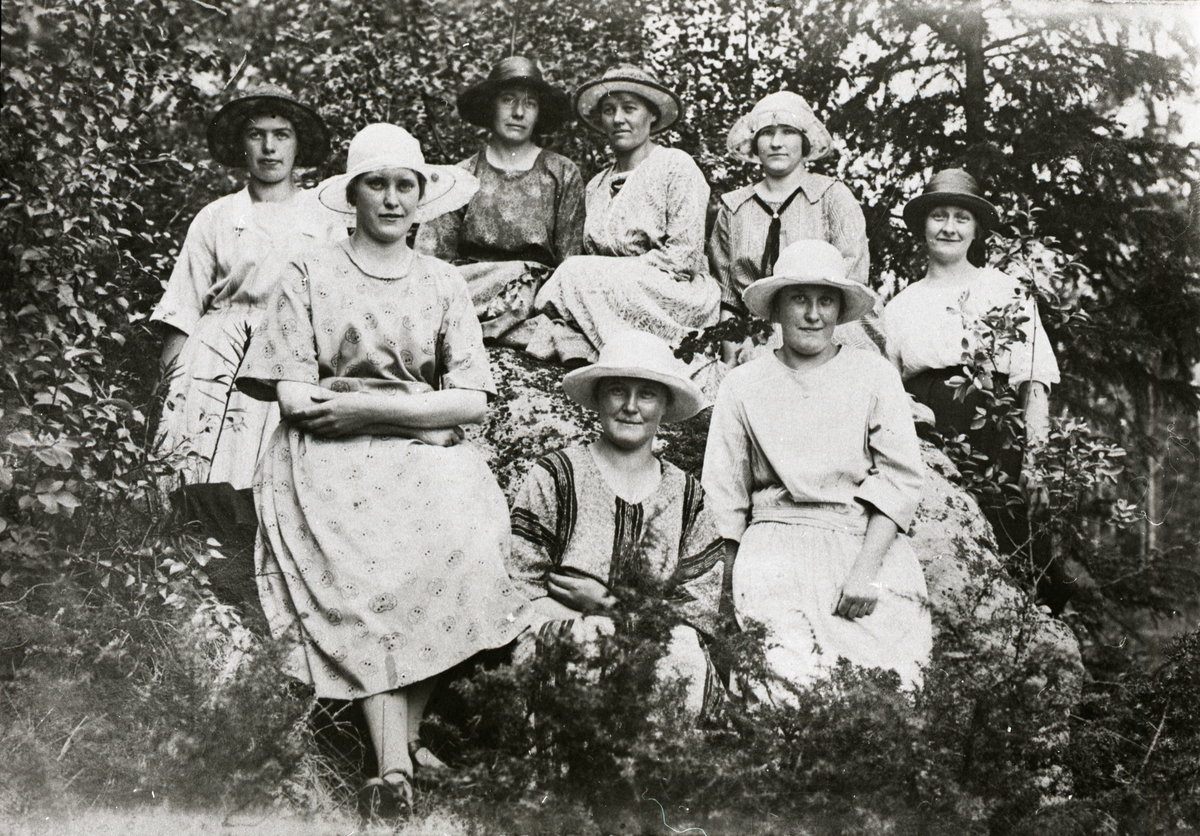 Gruppfoto av några damer iförda klänning och hatt i ett skogsbryn.