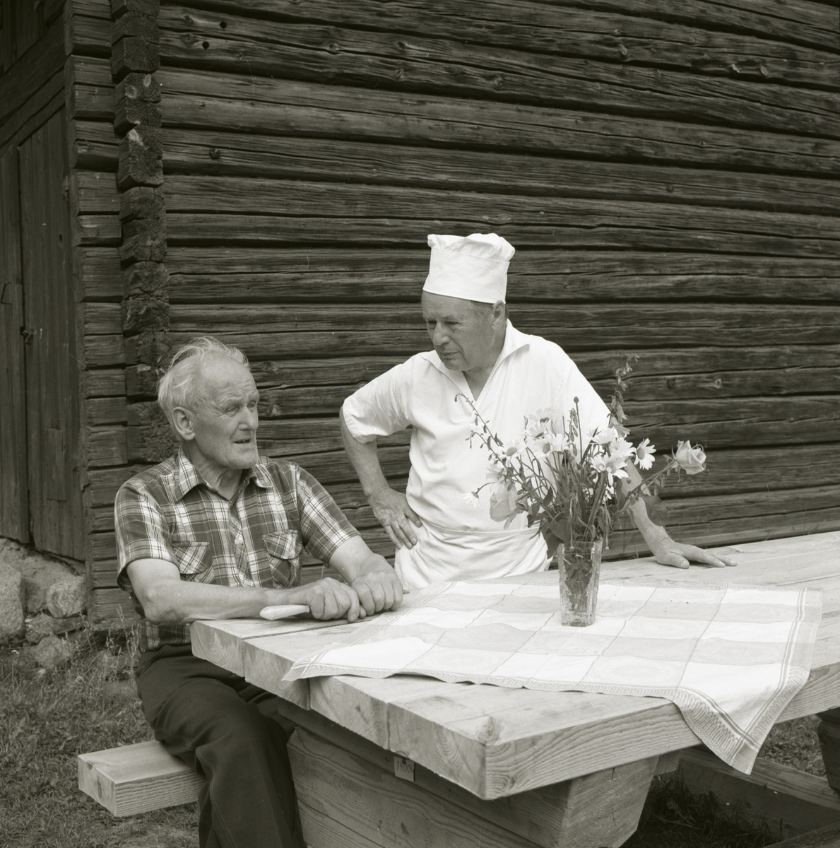 En man sitter vid ett bord och bredvid honom står en kock.